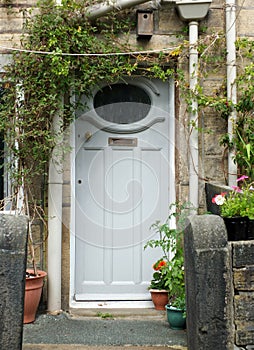 Traditional old blue grey painted wooden house door with brass letter box and window with a white frame surrounded flowers, pot