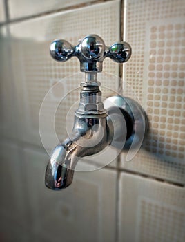 Traditional and old steel faucet attached on a tiled wall. photo