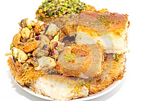 Traditional oriental sweets in white plate with different nuts on a white table, side view, close-up