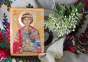 Traditional orthodox icon of St. George the Victorious. Handwritten icon on the background of Ukrainian rushnyks and lilies of the