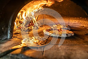 Traditional oven for baking pizza with burning wood and shovel. The cook rotates the pizza in the oven to ensure even baking