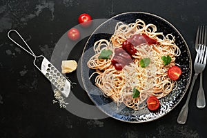 Traditional pasta spaghetti with tomato sauce, parmesan cheese and greens on a black stone background. Overhead view, flat lay