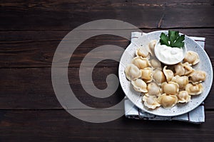 Traditional pelmeni, ravioli, dumplings filled with meat on plate, russian kitchen. Wooden rustic background, copy space
