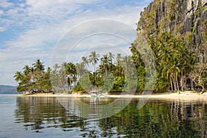 Traditional philippinian boat near idyllic beach with palm trees and mountain. Tropical landscape of Ellis island in Philippines.