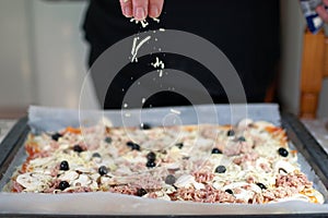 Traditional pizza cooking by italian chef at home. Adding some cheese