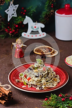 Traditional Polish Christmas dish, noodles with poppy seeds, raisins, candied fruits and sliced almonds on a red plate on a brown