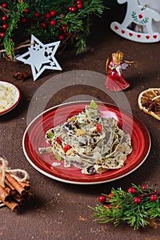 Traditional Polish Christmas dish, noodles with poppy seeds, raisins, candied fruits and sliced almonds on a red plate on a brown