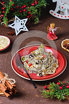 Traditional Polish Christmas dish, noodles with poppy seeds, raisins, candied fruits and sliced almonds on a red plate on a brown