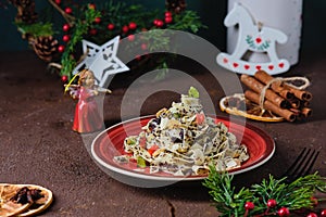 Traditional Polish Christmas dish, noodles with poppy seeds, raisins, candied fruits and sliced almonds on a red plate on a brown