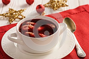 Traditional Polish christmas soup - red borscht soup with dumplings on white plate.