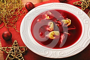 Traditional Polish christmas soup - red borscht soup with dumplings on white plate.