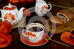 Traditional poppy seed bun with cup of tea and milk near poppies flowers and dishes with poppies ornaments. Delicious