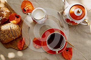 Traditional poppy seed bun with cup of tea and milk near poppies flowers and dishes with poppies ornaments. Delicious