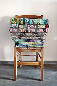 Traditional quilts stacked on wooden chair against neutral wall