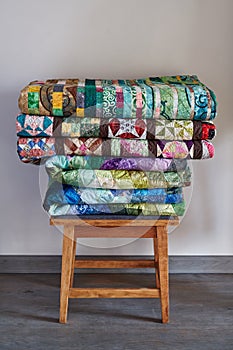 Traditional quilts stacked on wooden stool against neutral wall