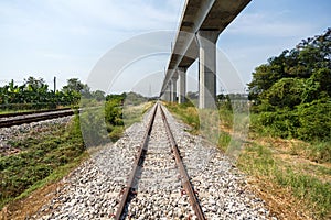 A traditional railway track lined with gravel ballast running parallel to a modern elevated rail. It showcases a juxtaposition