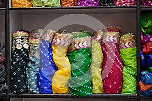 Traditional Rajasthan dress materials is neatly stacked for sale in a cloth merchant shop in India. Colorful fabric street stall.