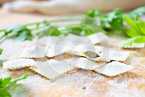Traditional raw ravioli with green and meat on a wooden table with flour