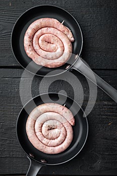 Traditional raw spiral pork sausages in cast iron frying pan  on black wooden table background  top view flat lay