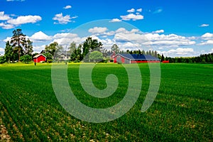 Traditional red farm house barn with white trim in open pasture with blue sky in Finland