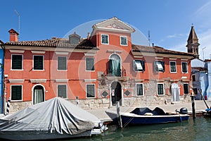 Traditional red house and modern boats in Burano, Venice, Italy