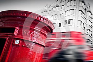 Traditional red mail letter box and red bus in motion in London, the UK.