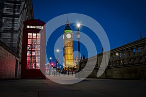 Traditional red phone booth or telephone box at night with Big Ben in the background, the famous english landmark in London,