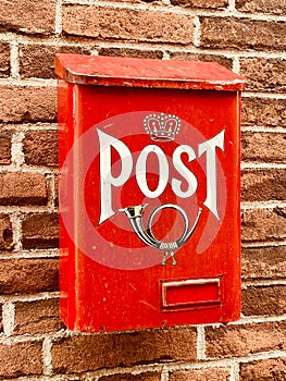 Traditional red postbox fixed on house brick wall by house entrance used for mail & letter delivery.