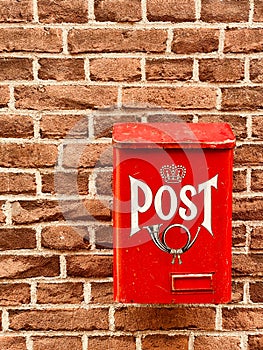 Traditional red postbox fixed on house brick wall by house entrance used for mail & letter delivery.