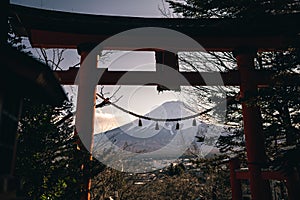 A traditional red torii gate and the Fuji mountain with snow cover at sunset