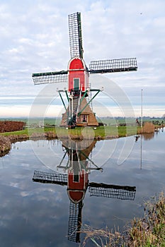 Traditional red wip windmill reflected in water, Holland landscape