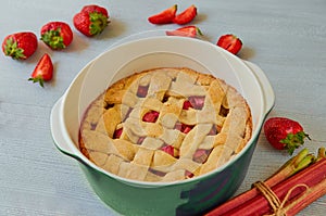 Traditional rhubarb strawberry pie in the baking dish on the gray kitchen table. Veggie tart decorated with organic strawberries
