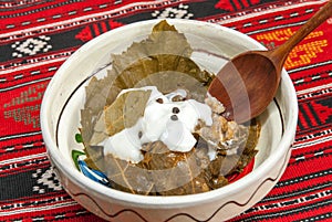 Traditional romanian and balkanic dish minced meat wrapped in vine leafs served with cream in a clay bowl photo