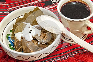 Traditional romanian and balkanic dish minced meat wrapped in vine leafs served with cream in a clay bowl photo