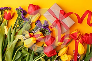 Traditional Romantic background with bouquet of red tulips and gift box on yellow, Top view with copy space, banner, flyer,