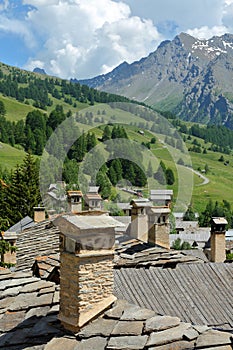 Traditional roofs and chimneys in Saint Veran village, with mountain range covered with snow and pine tree forests