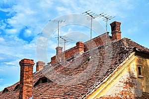 Traditional roofs in Sibiu, Romania, with eye shaped windows, brick chimneys and old TV antennas on top, on a bright day.