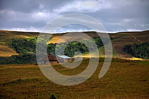 Traditional round hut with smoke from cooking fire in savanna with awesome patches of light on the grass