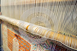 A traditional rug being woven on a carpet vertical loom, showing wool pile under tension, foundation, warp and weft