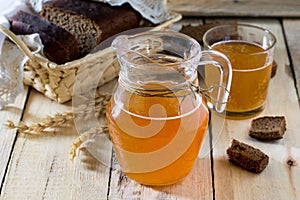 Traditional Russian cold rye drink Kvas in a glass and a jug on the kitchen table in a rustic style.