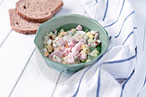 Traditional russian cold soup okroshka with some of its cooking components on a white wooden background with bread