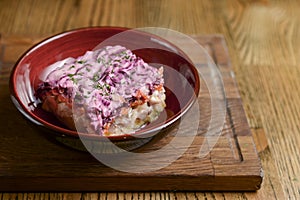 Traditional Russian herring salad served in a bowl on dark wooden table background in a restaurant.