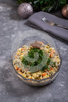 Traditional Russian Olivier salad in glass bowl on gray background. Holiday salad looks like Christmas tree