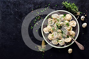 Traditional russian pelmeni, ravioli, dumplings with meat on black concrete background. Parsley, quail eggs, pepper photo