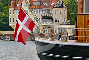 Traditional sailing ship with large Danish national flag hanging from the stern in the harbor of Sonderborg, Denmark