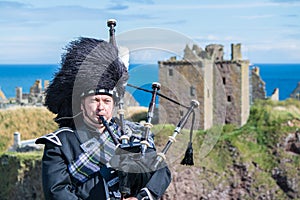 Traditional scottish bagpiper in full dress code at Dunnottar Castle