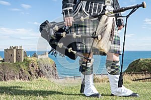 Traditional scottish bagpiper in full dress code at Dunnottar Castle