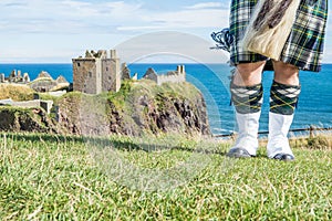 Traditional scottish bagpiper in full dress code at Dunnottar Castle