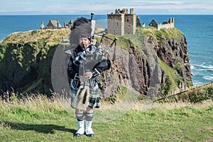 Traditional scottish bagpiper in full dress code at Dunnottar Castle