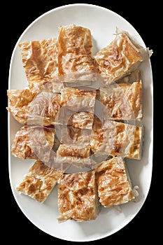 Traditional Serbian Savory Crumpled Cheese Pie Gibanica Served on White Oval Ceramic Tray Isolated on Black Background